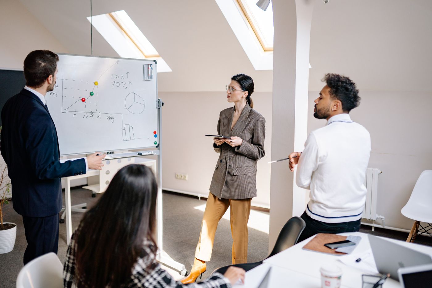 Équipe en réunion dans une salle lumineuse, tableau avec graphiques, ambiance collaborative