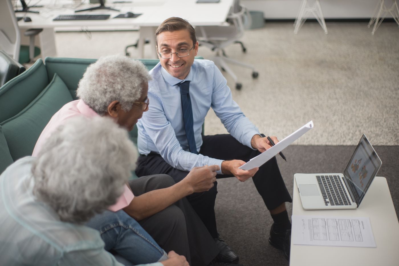 Conseiller présentant un document à deux personnes lors d'un entretien, ordinateur portable et documents sur la table, ambiance chaleureuse
